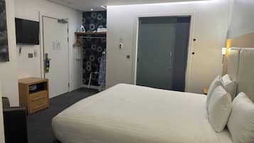 A hotel room with a bed, a wardrobe, a TV, and a small desk with drawers.