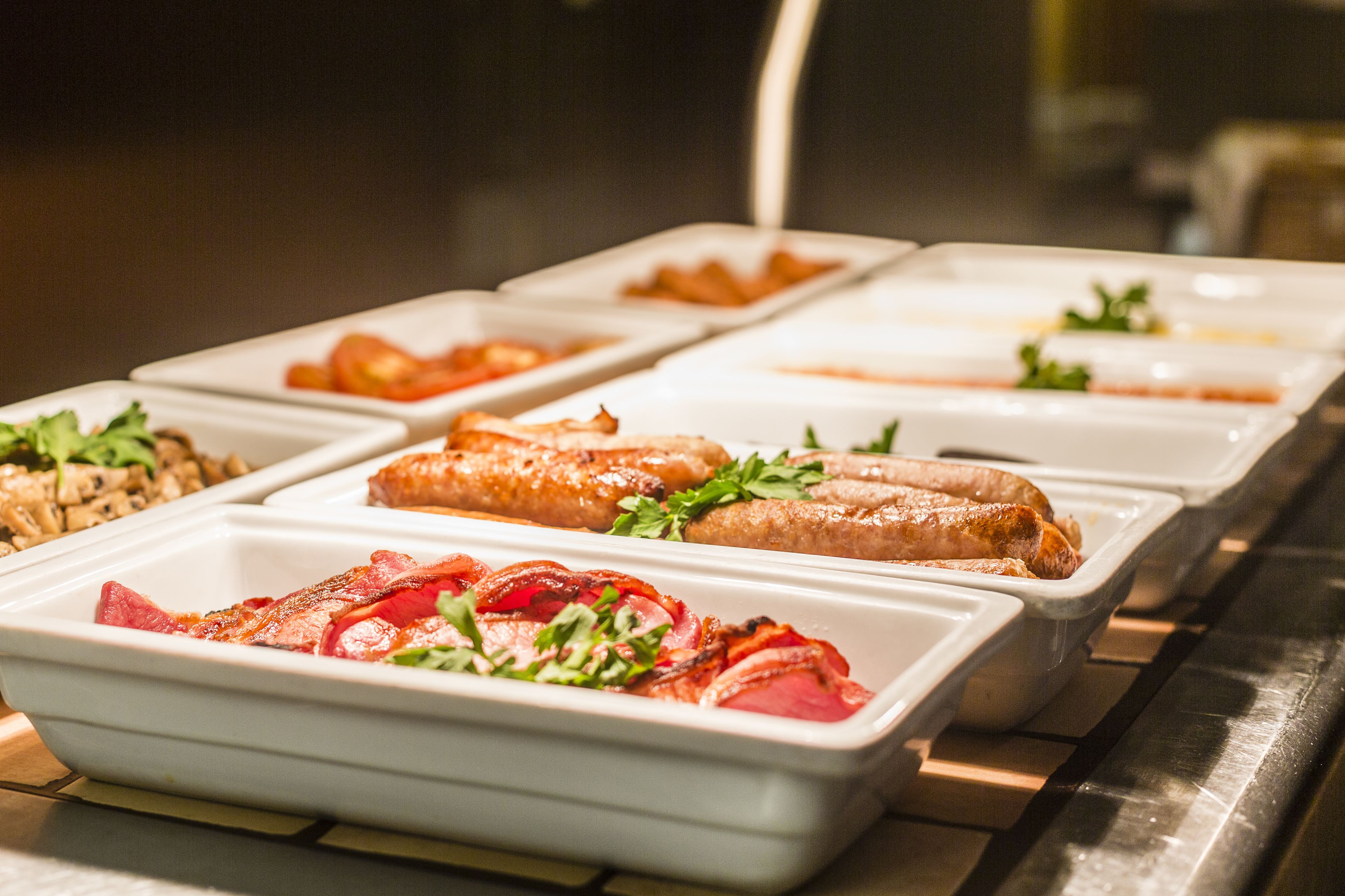Un bufé con diversos alimentos, incluyendo carnes y ensaladas, en fuentes blancas.