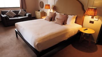 Una cama bien hecha con almohadas, un sofá con cojines, una mesita de noche con lámpara, y una mesita auxiliar con lámpara.