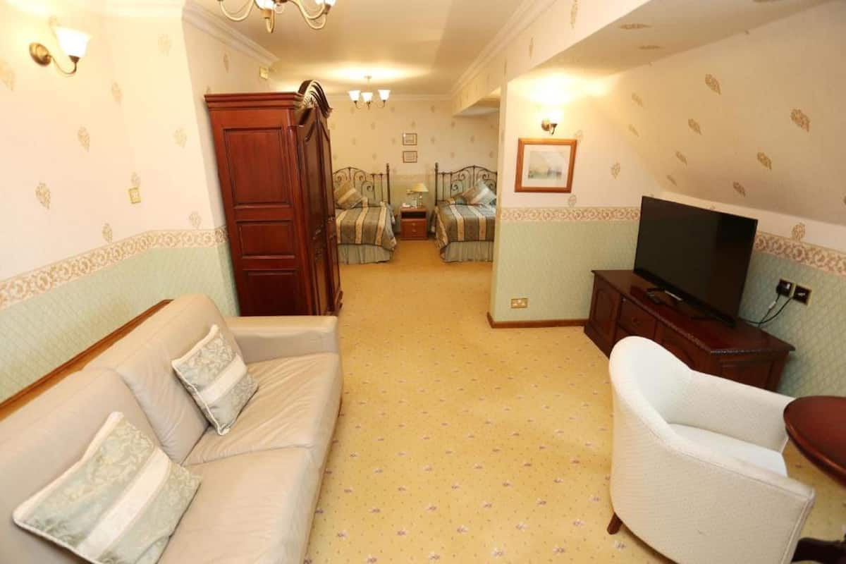 Quarto de hotel com sofá, uma cadeira, televisão e duas camas com roupa de cama combinando.