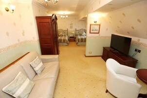 A hotel room with a sofa, a chair, a TV, and two beds with matching bedding.