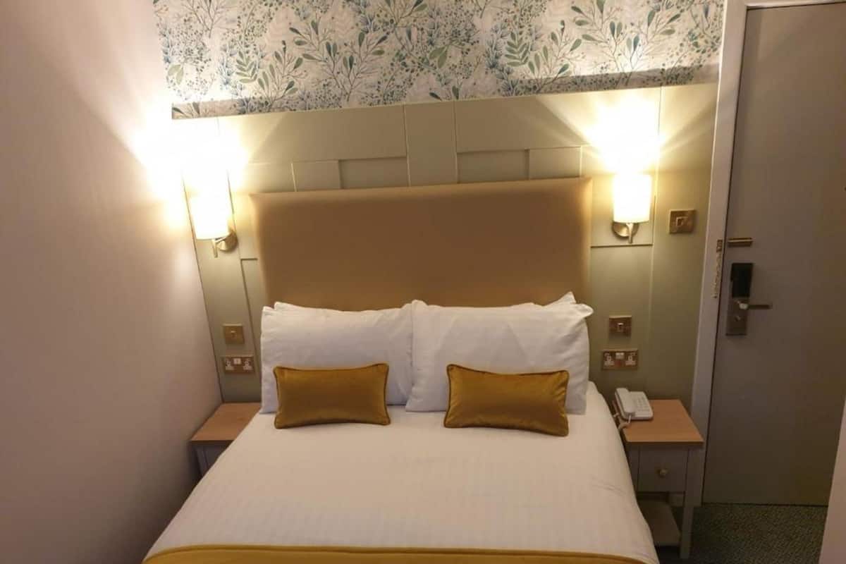 Quarto de hotel com cama, duas mesas de cabeceira e uma porta.