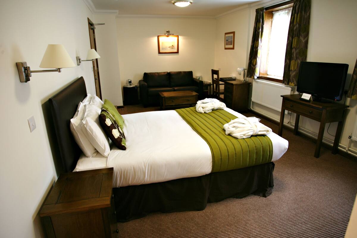 Quarto de hotel com cama, sofá, televisão e janela com cortinas.