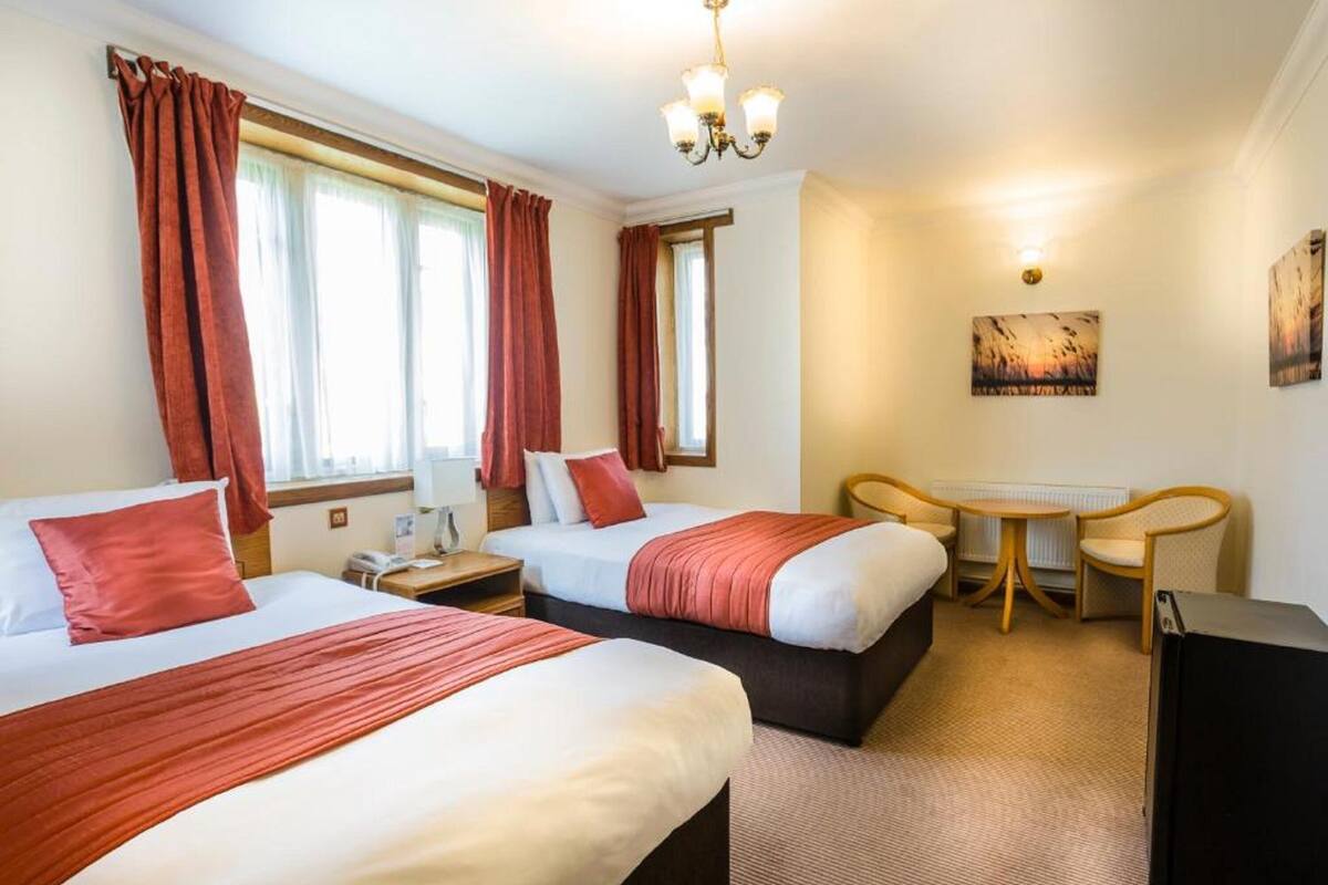 Quarto de hotel com duas camas, uma escrivaninha, uma cadeira e uma televisão.