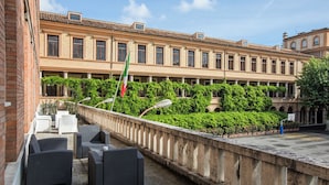A courtyard with outdoor seating, a flag, and a building with classical architecture. - Mercure Roma Centro St. John (Rome)