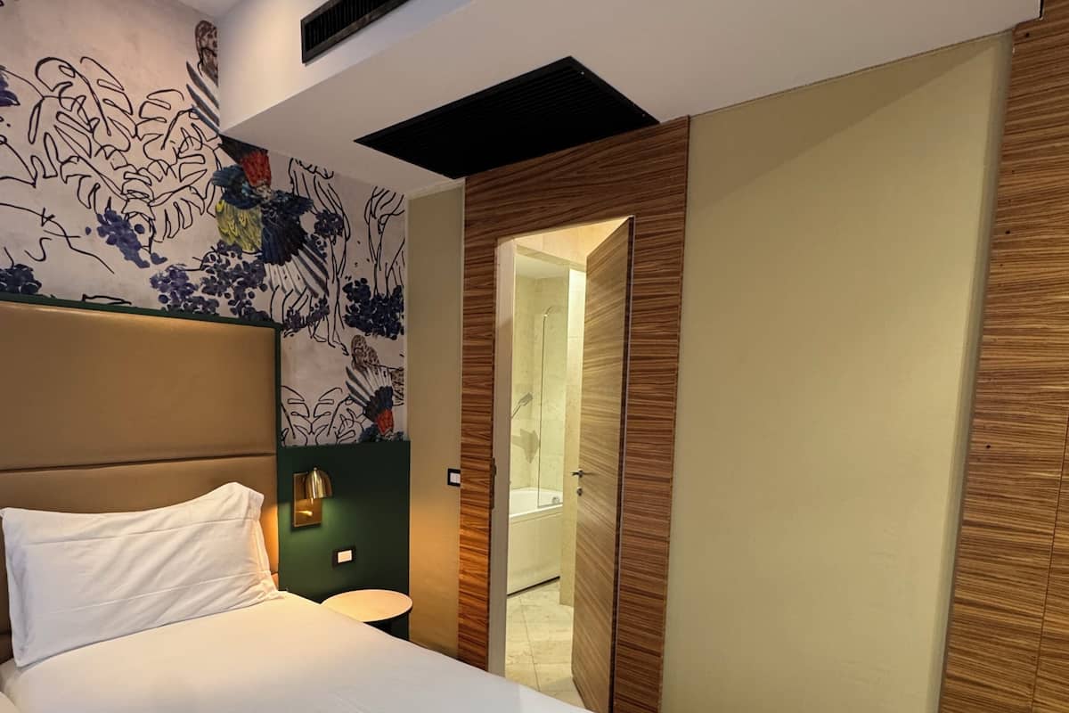 A modern hotel room with a large bed, a bathroom visible through an open door, and a decorative wall mural.