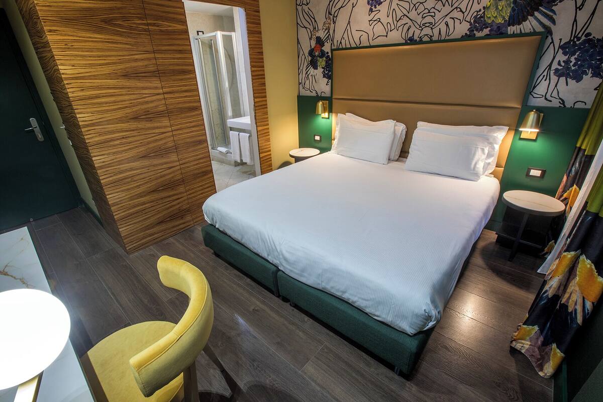 A hotel room with a bed, bedside tables, a chair, a shower, and a wall with a floral pattern.