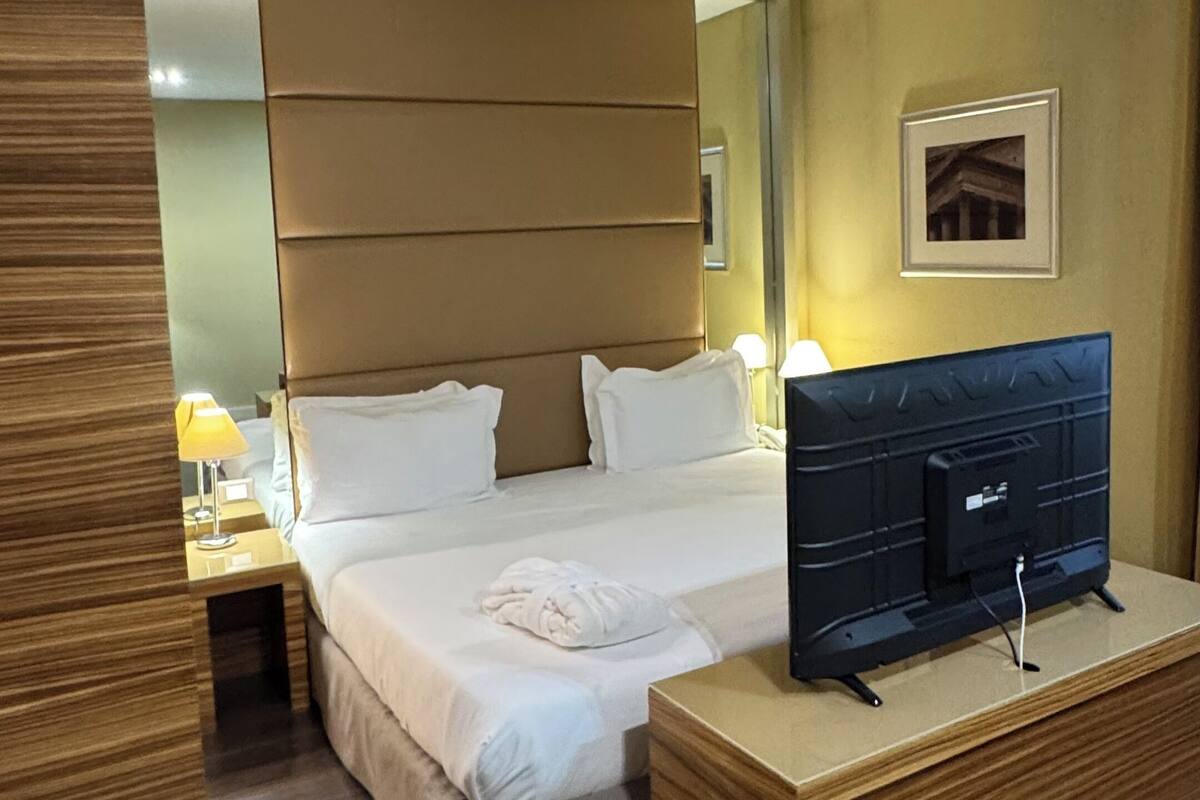 A hotel room with a bed, bedside table, TV, and a mirror.