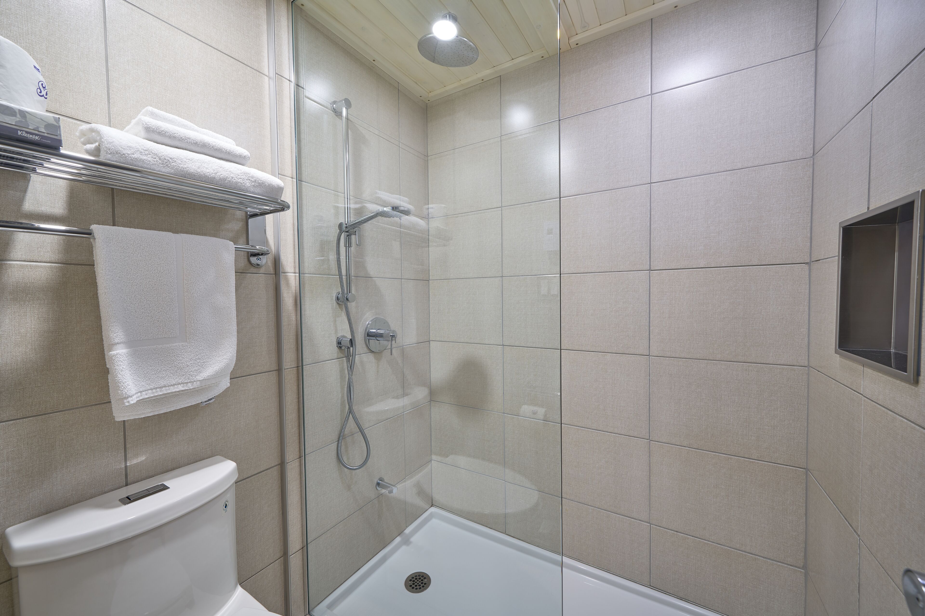 A modern bathroom with a glass-enclosed shower, a white toilet, and a towel rack with folded towels.