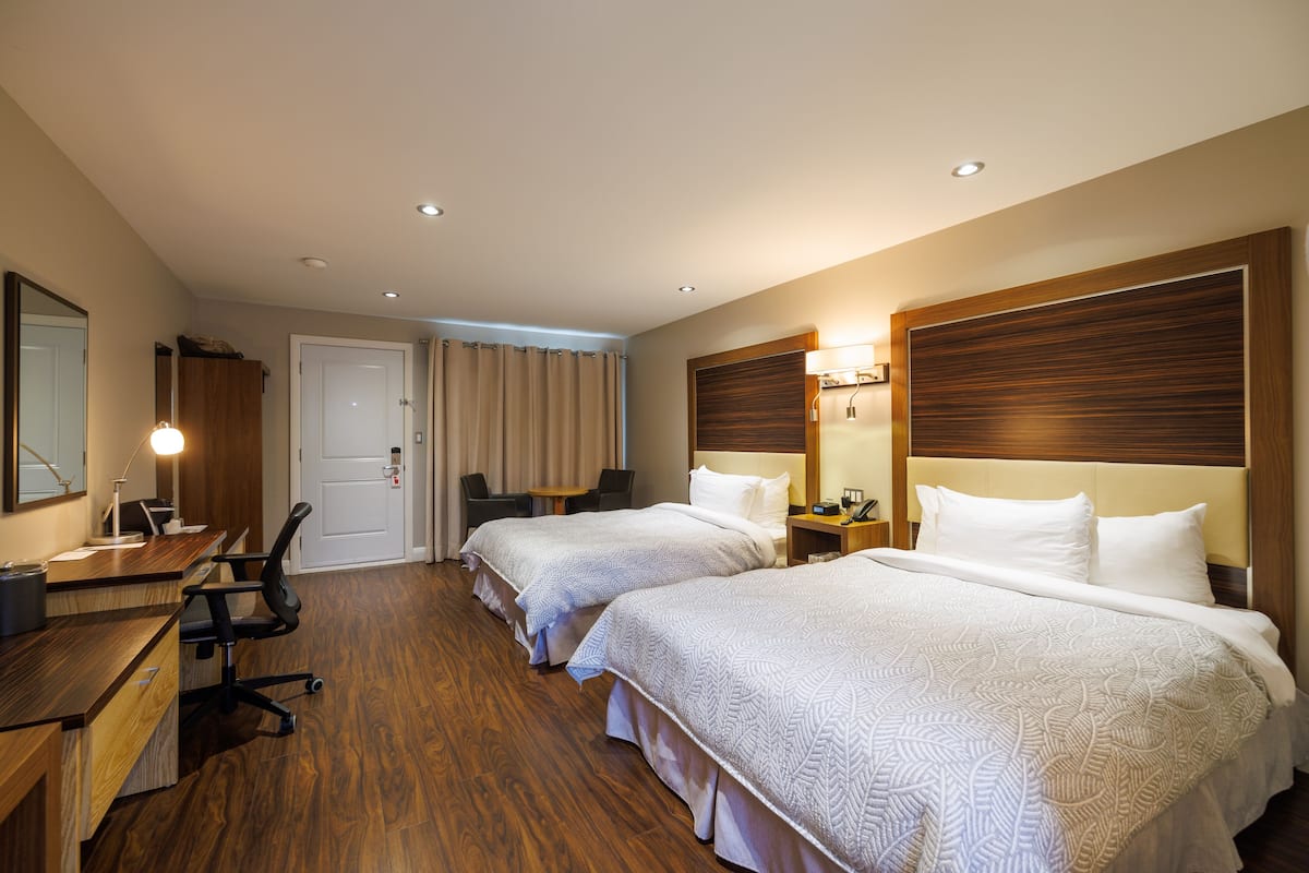 Ett hotellrum med två sängar, ett skrivbord med en stol, en spegel och en dörr.