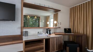 A modern hotel room with a wooden vanity, a flat-screen TV, a laptop, and a large mirror.