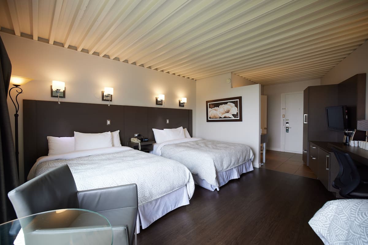Ett hotellrum med två sängar, ett skrivbord, en stol, en tv och en inramad tavla på väggen.