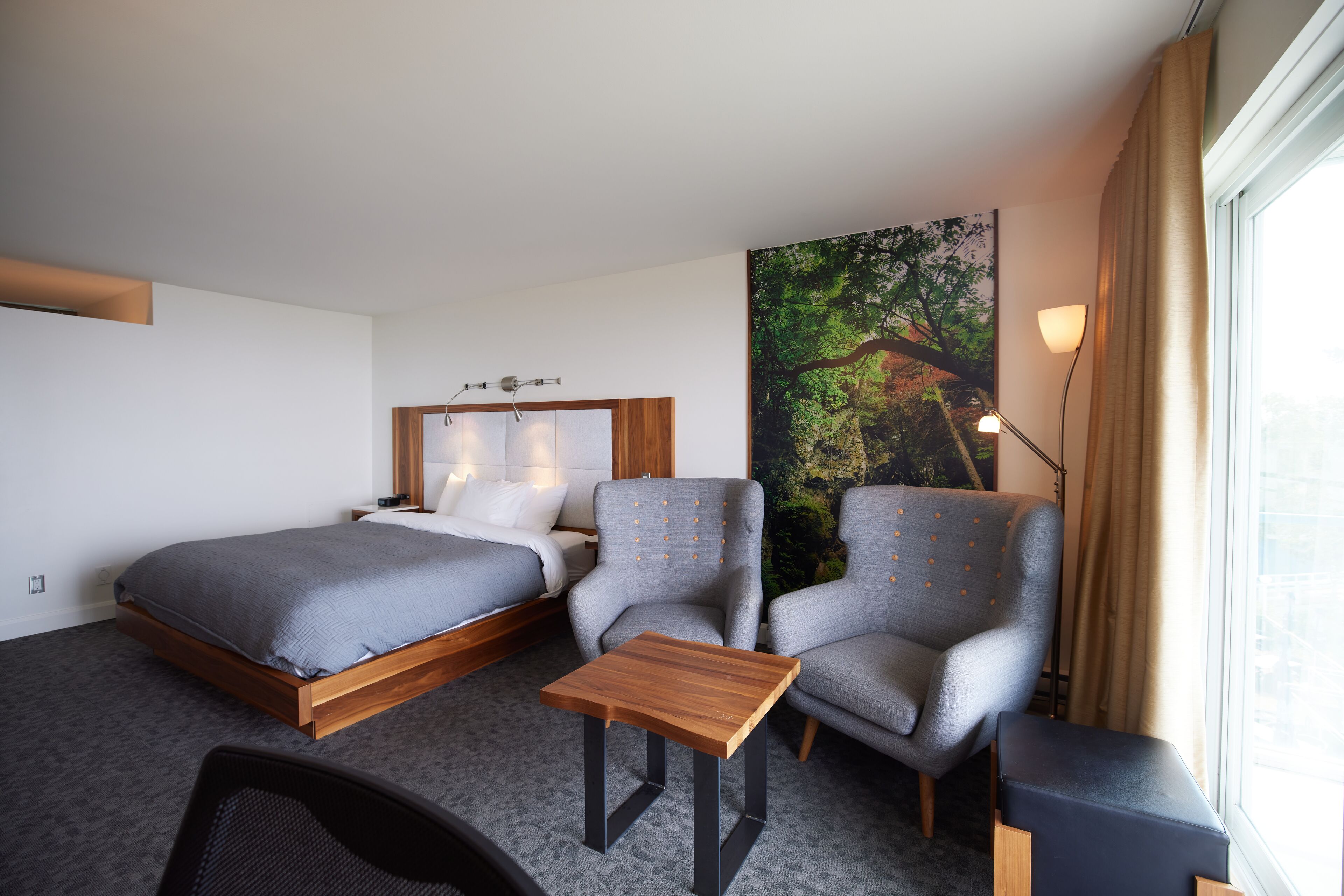 Una habitación de hotel con una cama, dos sillones, una mesita y un ventanal con cortinas.