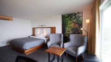 Una habitación de hotel con una cama, dos sillones, una mesita y un ventanal con cortinas.
