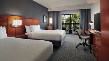 A hotel room with two beds, a desk, a chair, a TV, and a balcony with a view.