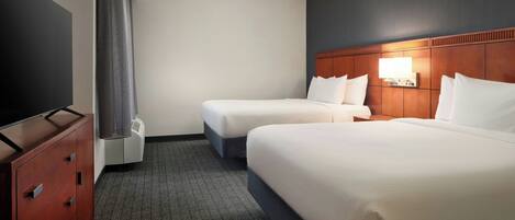 A hotel room with two beds, a TV, a dresser, and a wall-mounted light.