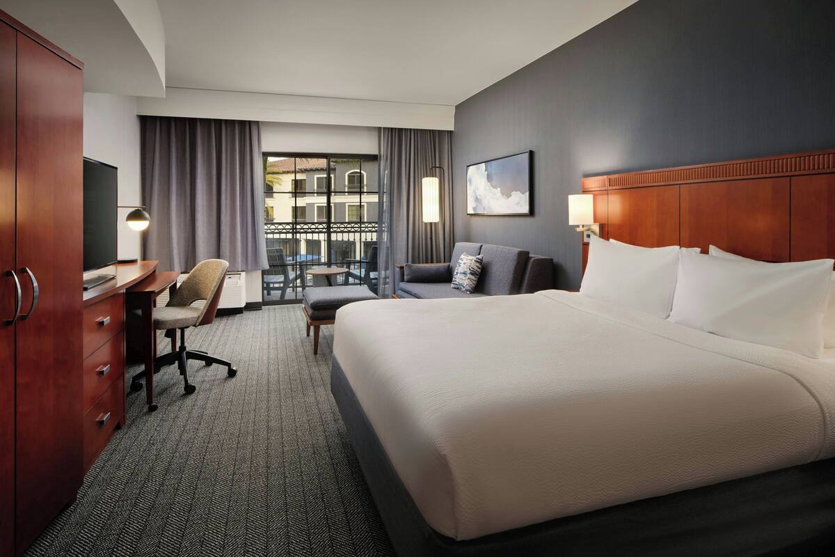 Une chambre d’hôtel avec un grand lit, un bureau avec une chaise, une télévision et un balcon avec vue.