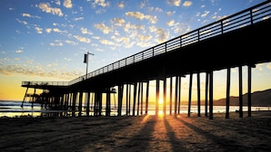 Un muelle se adentra en el océano al atardecer, bajo un cielo despejado.