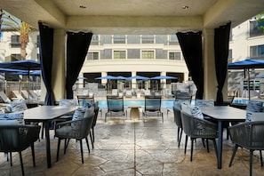 An outdoor pool area with lounge chairs and umbrellas, a stone-tiled floor, and a view of a building with balconies. - Courtyard by Marriott San Luis Obispo (San Luis Obispo)