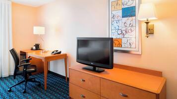 A hotel room with a desk, chair, television, and a framed artwork on the wall.