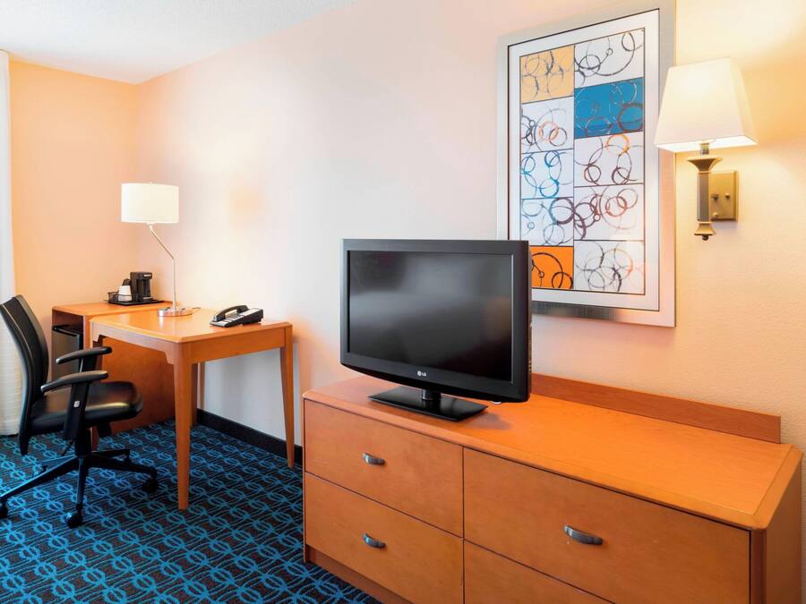 A hotel room with a desk, chair, television, and a framed artwork on the wall.