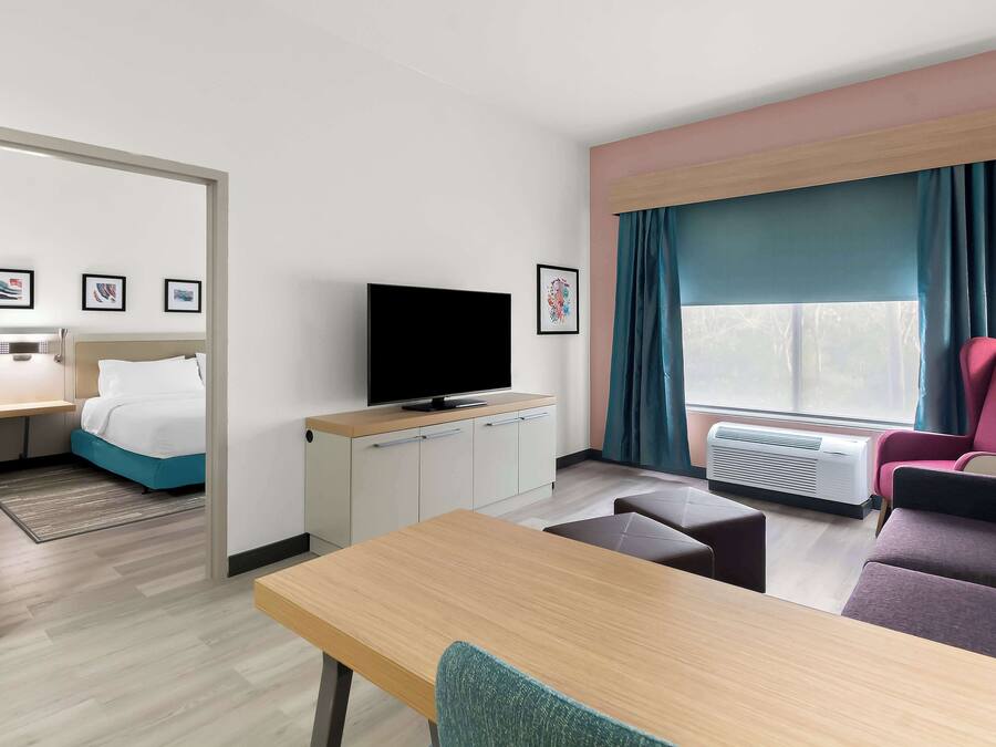 Una camera d'albergo con un letto, una televisione, una scrivania, una sedia, un divano e un'ampia finestra con tende.