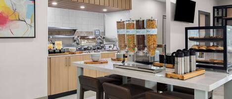A modern kitchen area with a coffee station, food dispensers, and a display case with baked goods.