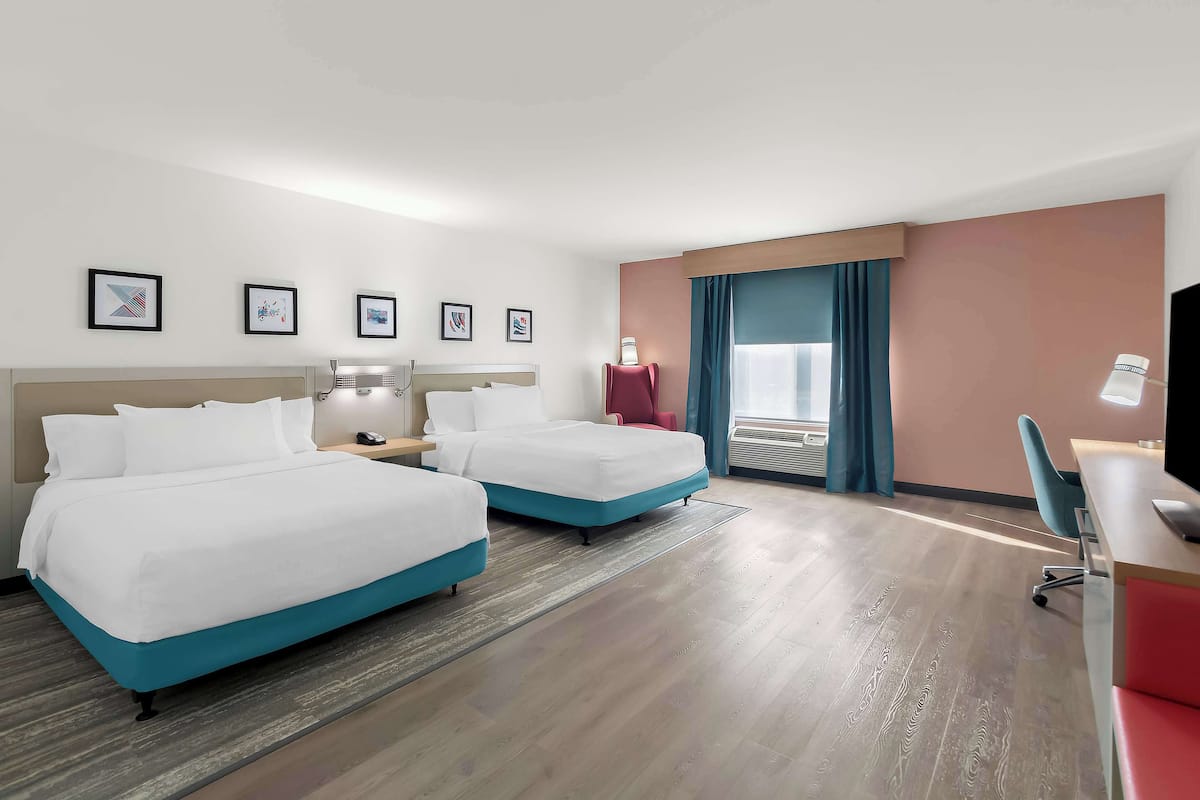 Ein Hotelzimmer mit zwei Betten, einem Schreibtisch, einem Stuhl und einem Fenster mit Vorhängen.
