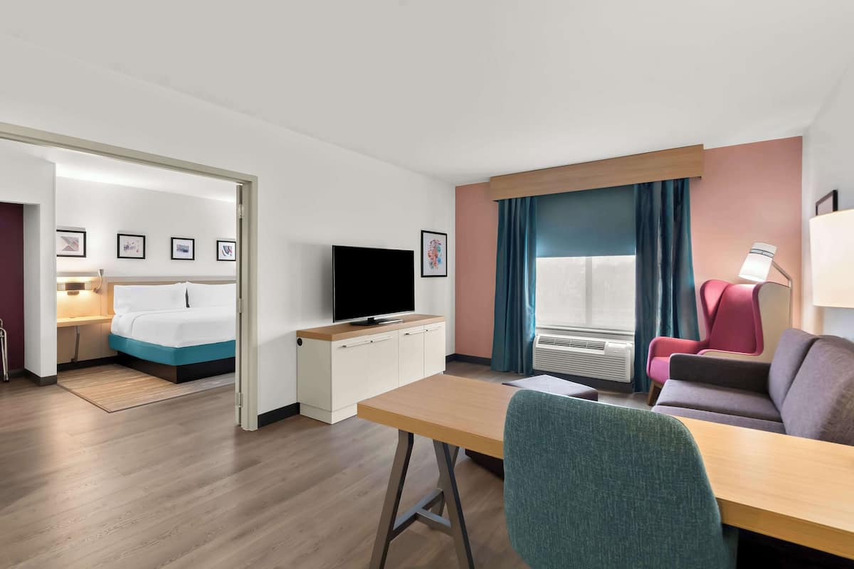 Ein Hotelzimmer mit Bett, Schreibtisch mit Fernseher, Stuhl und einer Couch.