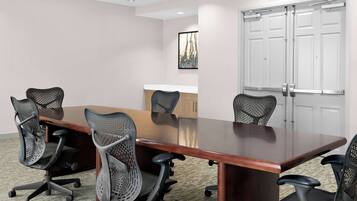A conference room with a long table, six mesh office chairs, a whiteboard, and a door with a handle.