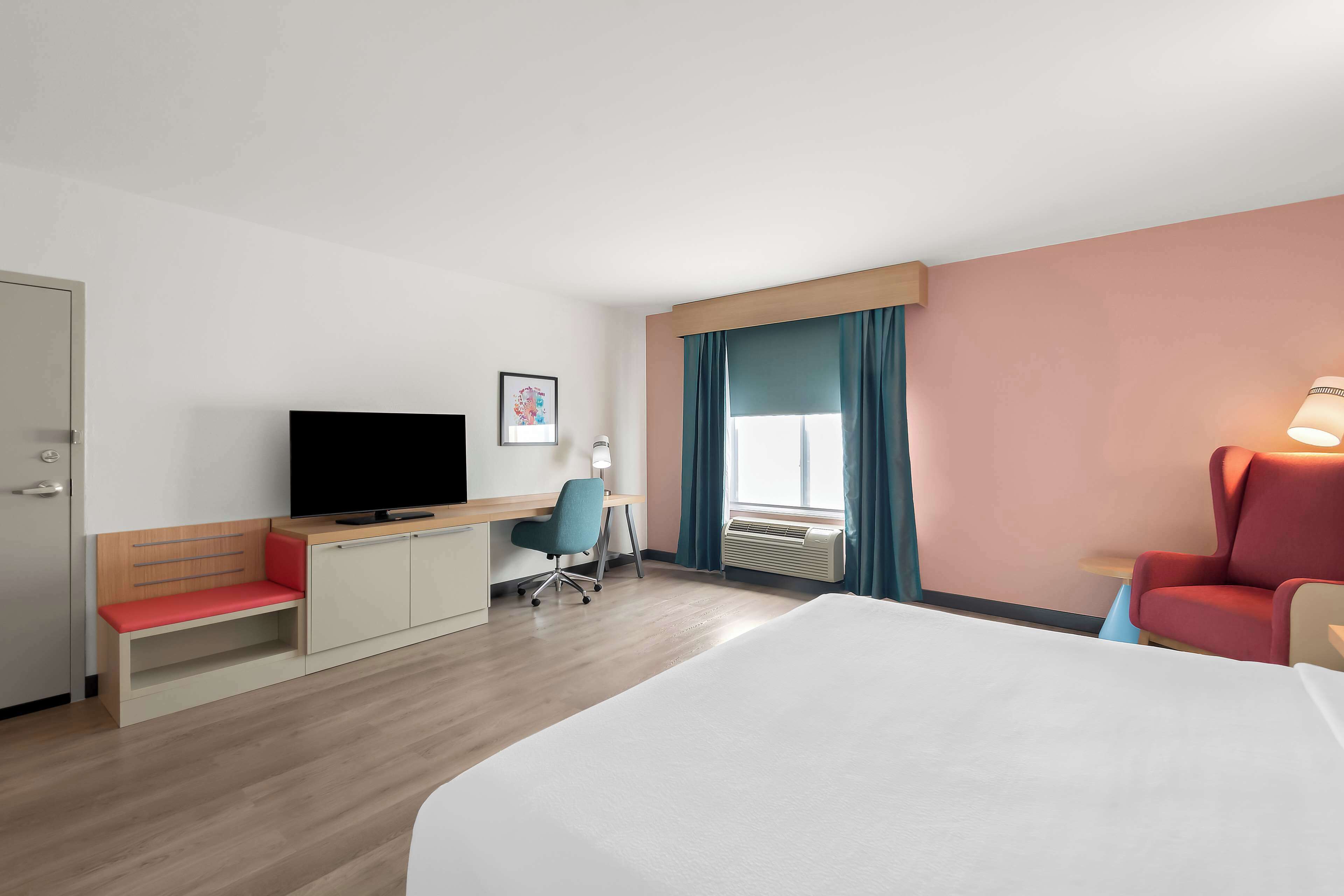 A hotel room with a bed, a desk with a chair, a television, and a window with curtains.