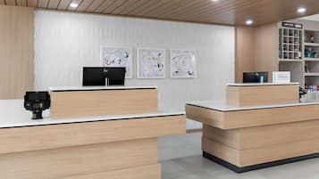 A hotel reception desk with a digital kiosk, a computer, and a sign indicating the hotel name.