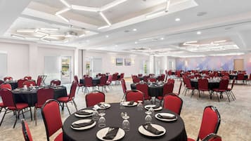 Un amplio salón de conferencias con mesas redondas, sillas rojas y un diseño moderno en el techo.