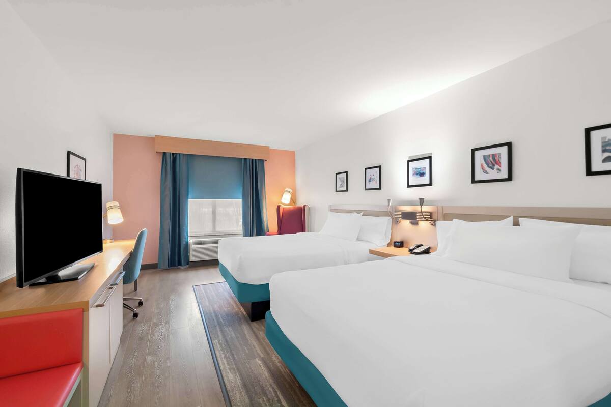 Ein Hotelzimmer mit zwei Betten, einem Fernseher, einem Schreibtisch und einem Stuhl.