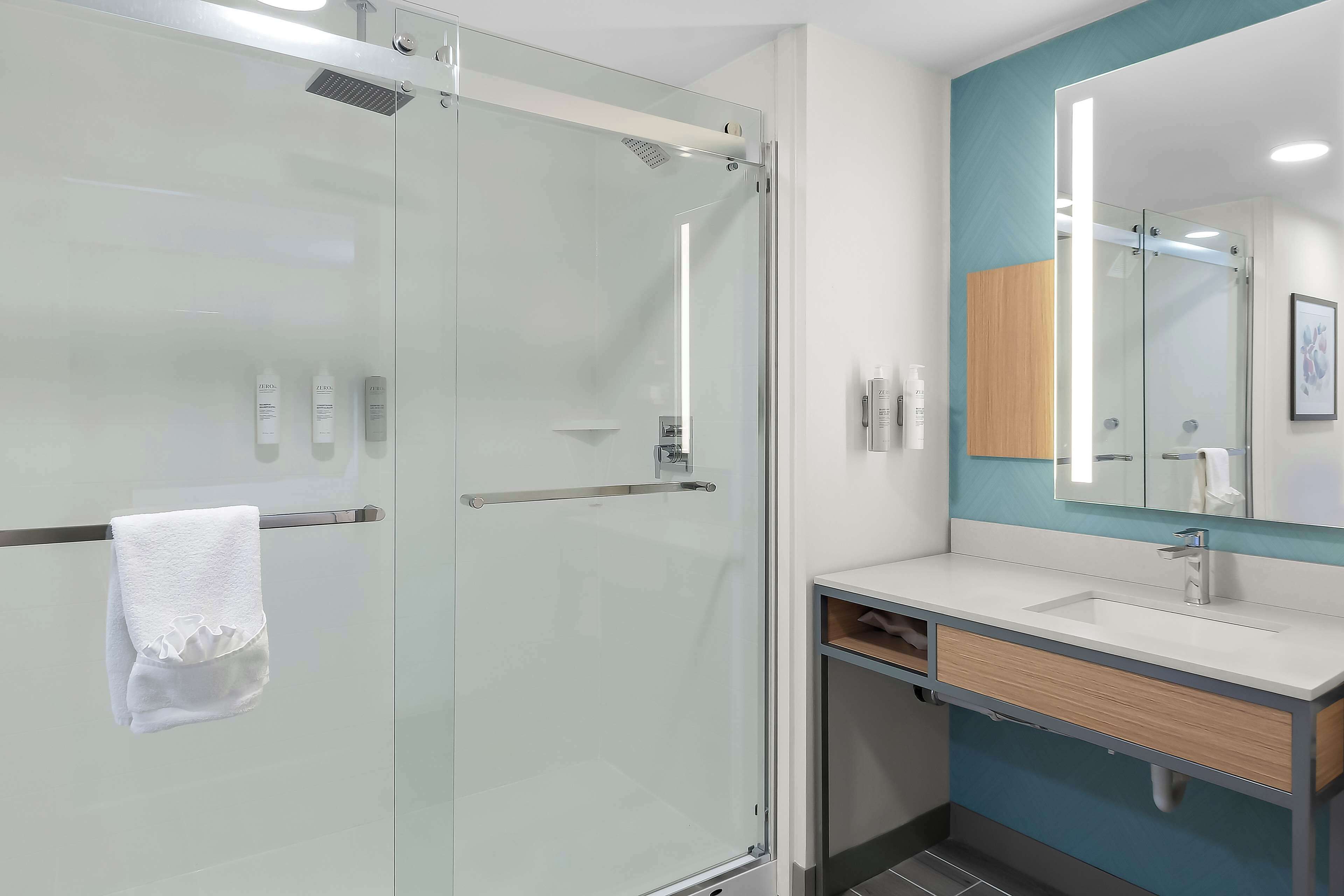 A modern bathroom with a glass-enclosed shower, a white sink, and a mirror with a wooden cabinet above it.