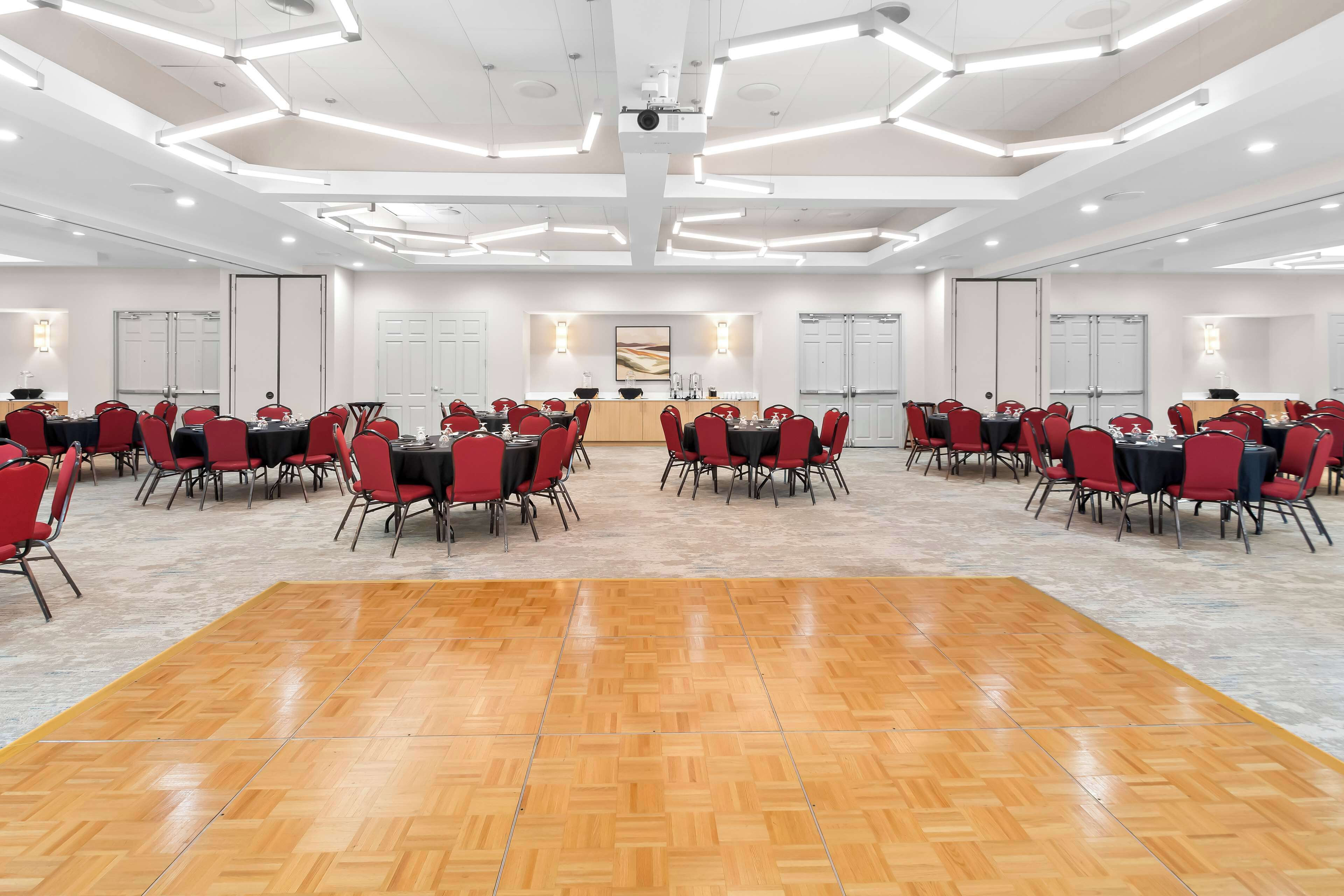 A conference room with a central table, surrounded by red chairs, and a wooden dance floor.