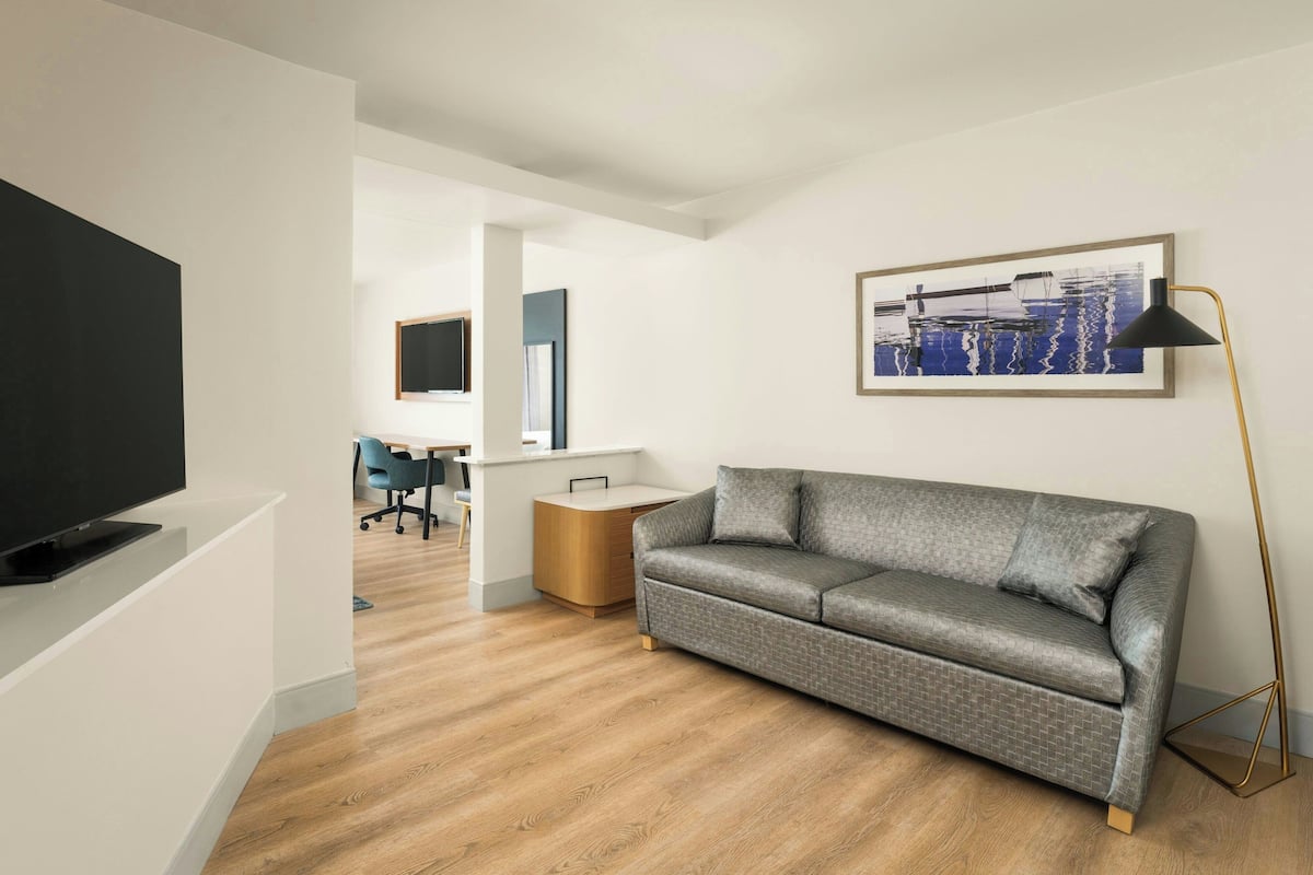 A modern living room with a grey sofa, a flat-screen TV, a coffee table, and a framed artwork on the wall.