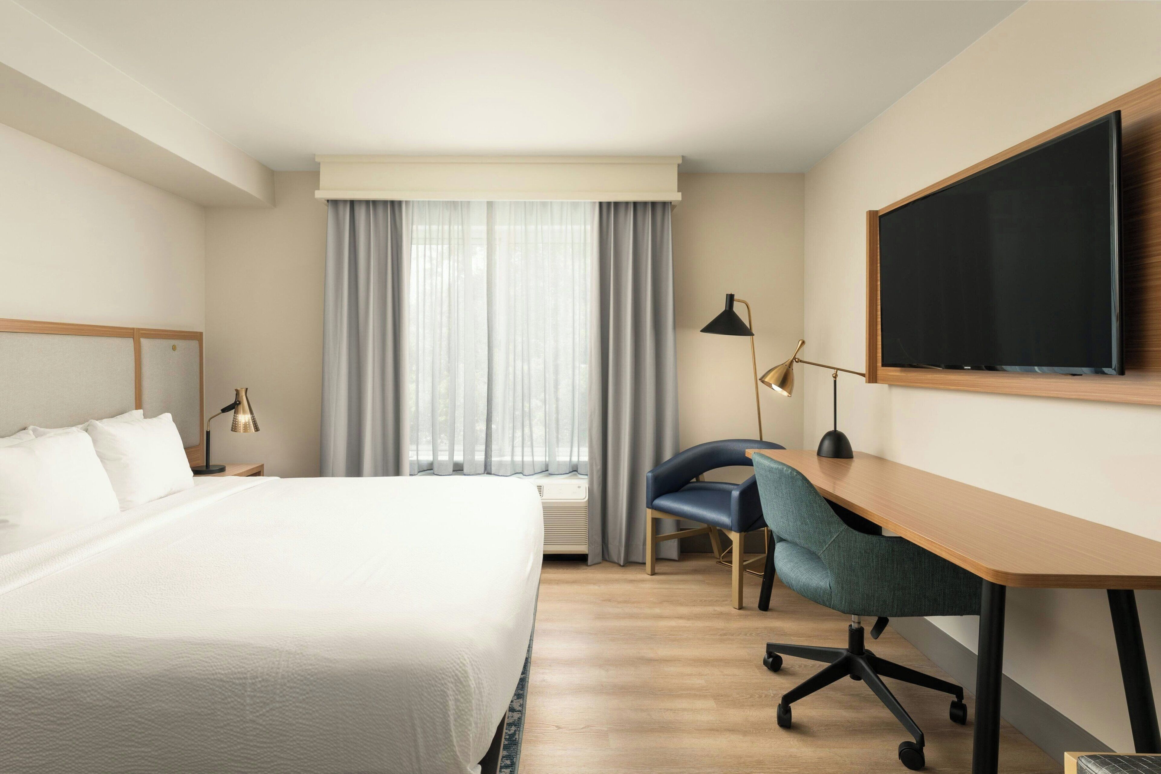 Et hotelværelse med en stor seng, et skrivebord med stol, et fladskærms-tv og et vindue med gardiner.