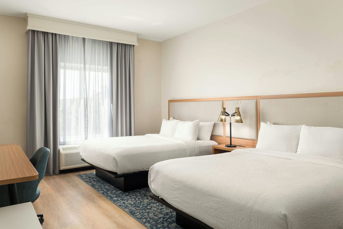 A hotel room with two beds, a desk, a chair, and a window with curtains.