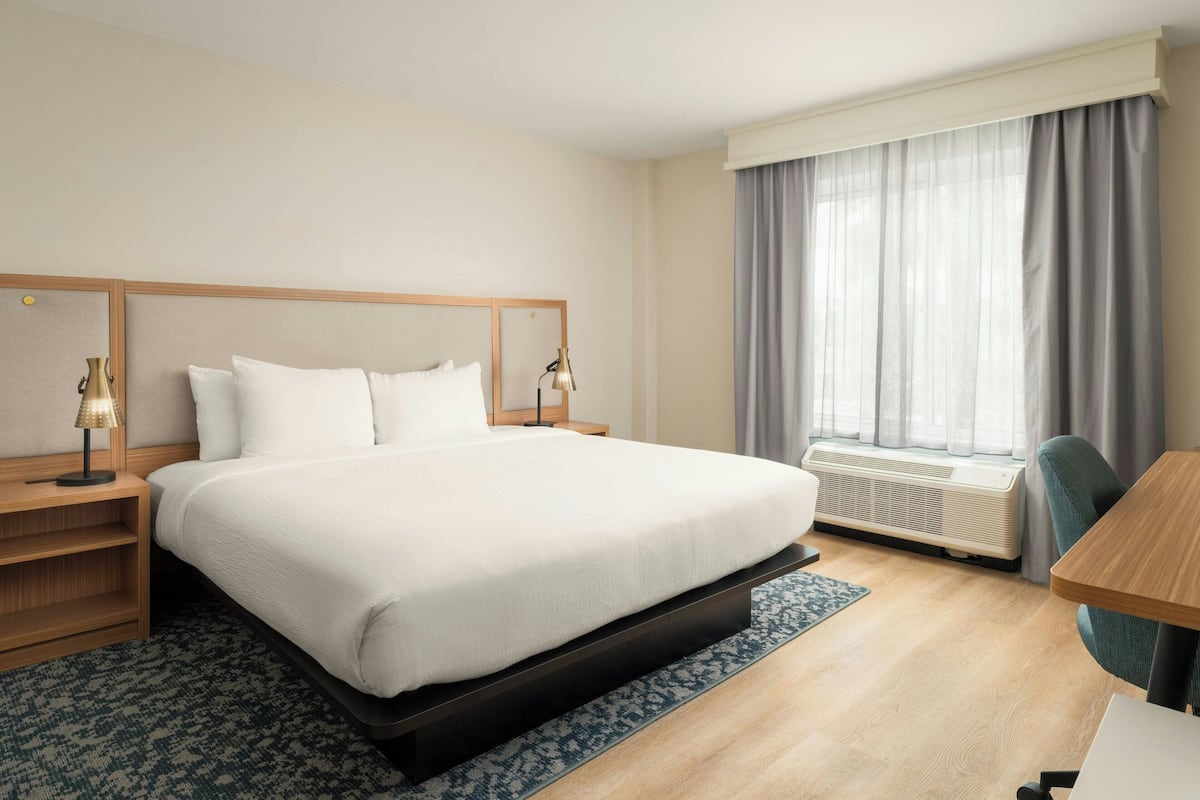 A hotel room with a large bed, bedside tables with lamps, a window with curtains, a desk, and a chair.