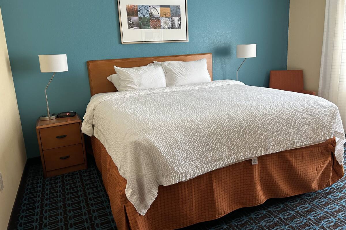A neatly made bed with a white quilt, a wooden headboard, and two bedside lamps.