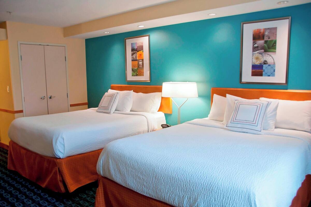 A hotel room with two beds, a nightstand, a lamp, and two framed pictures on the wall.