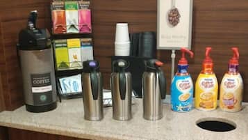 A coffee station with a coffee maker, disposable cups, and coffee mugs.