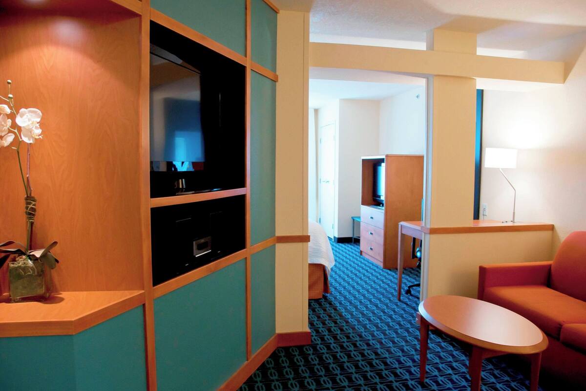 A hotel room with a TV, a small table, a sofa, and a decorative vase with flowers.