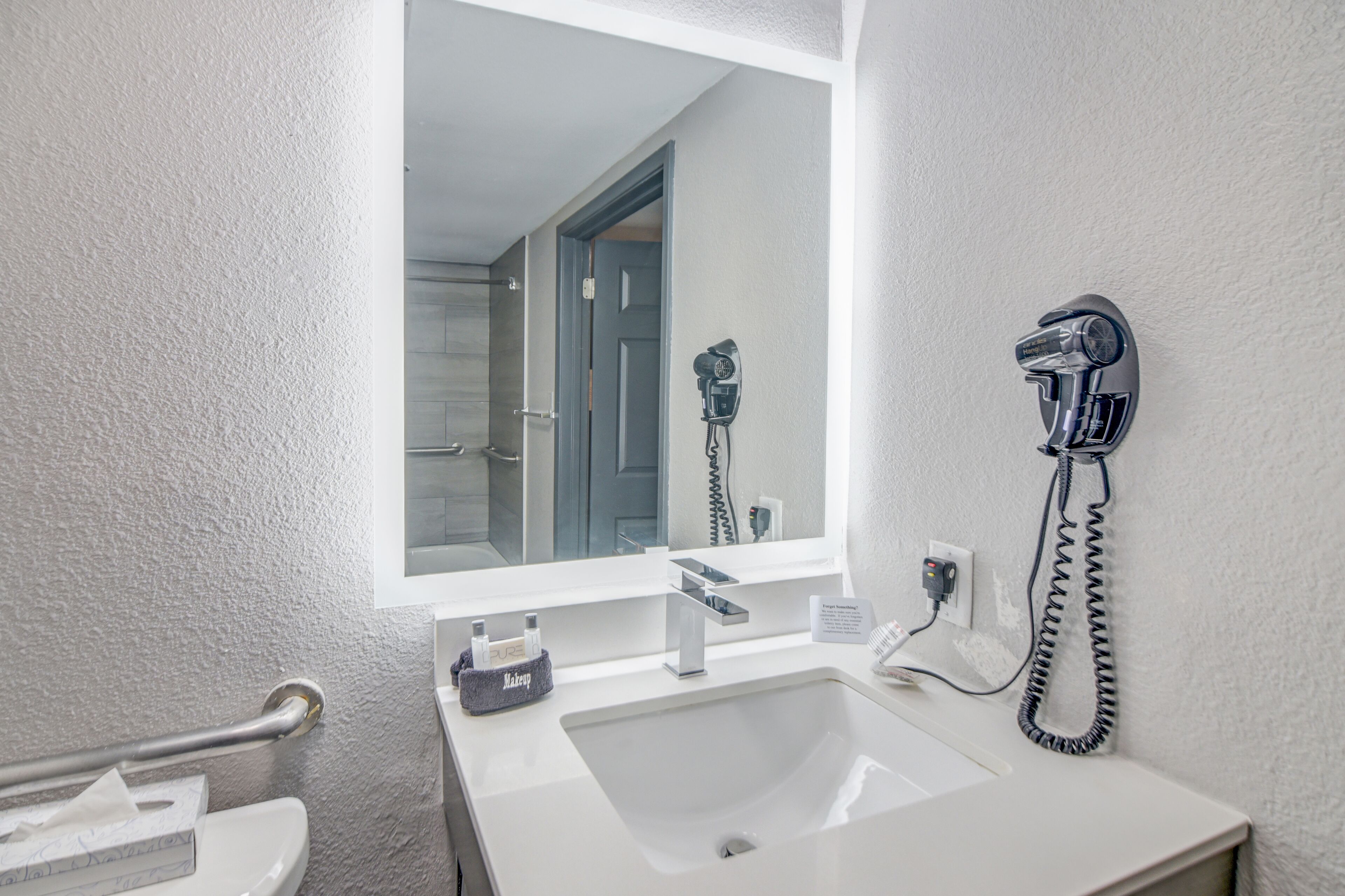 Een badkamer met een witte wastafel, een spiegel, een haardroger en een handdoekhouder.