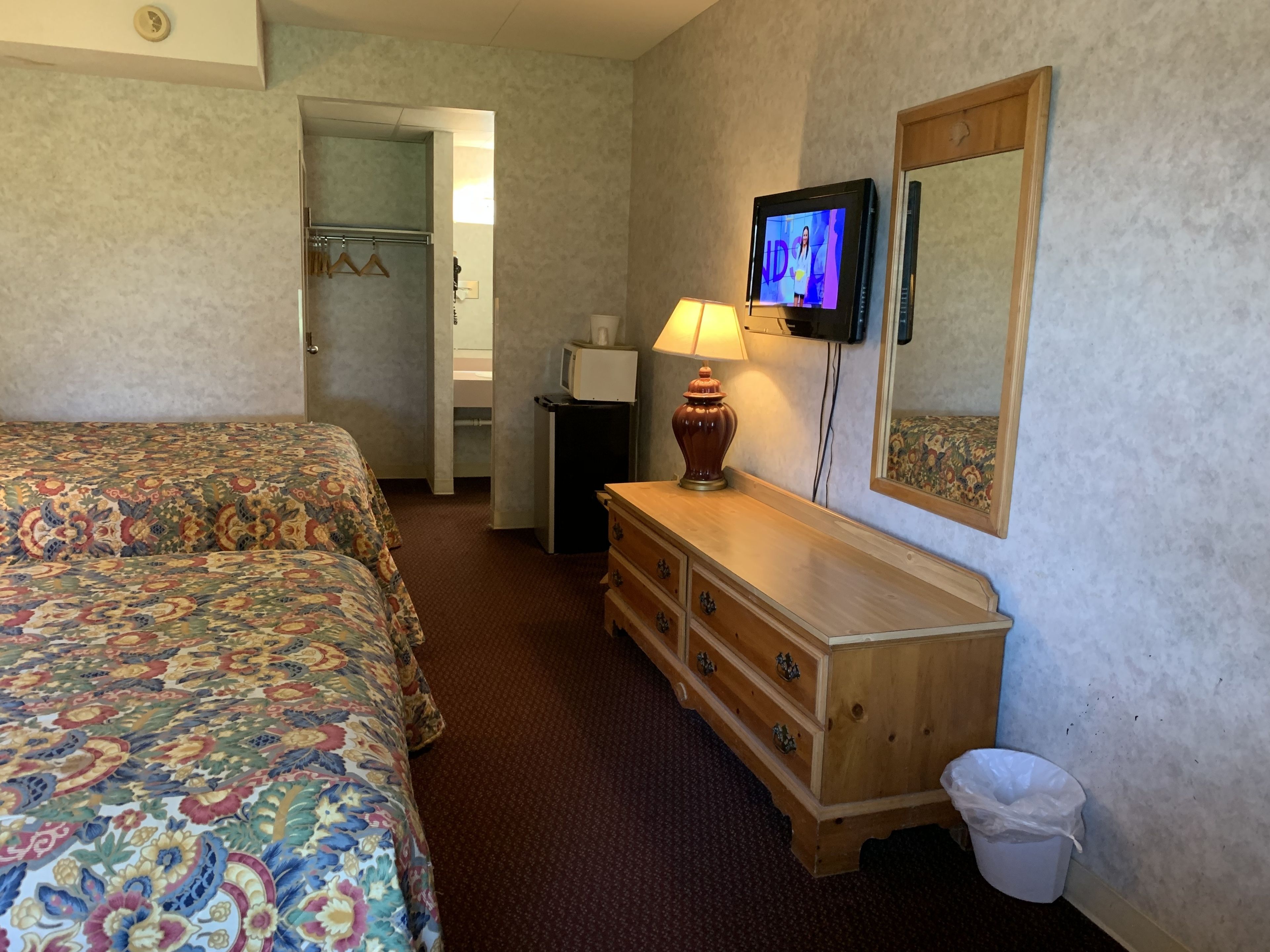 A hotel room with two beds, a television, a dresser, a lamp, and a mirror.