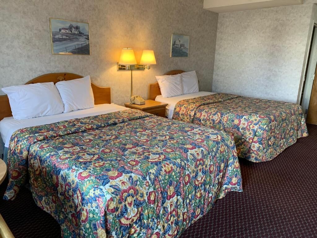 A hotel room with two beds, each with a floral bedspread, a nightstand with a lamp, and a painting on the wall.