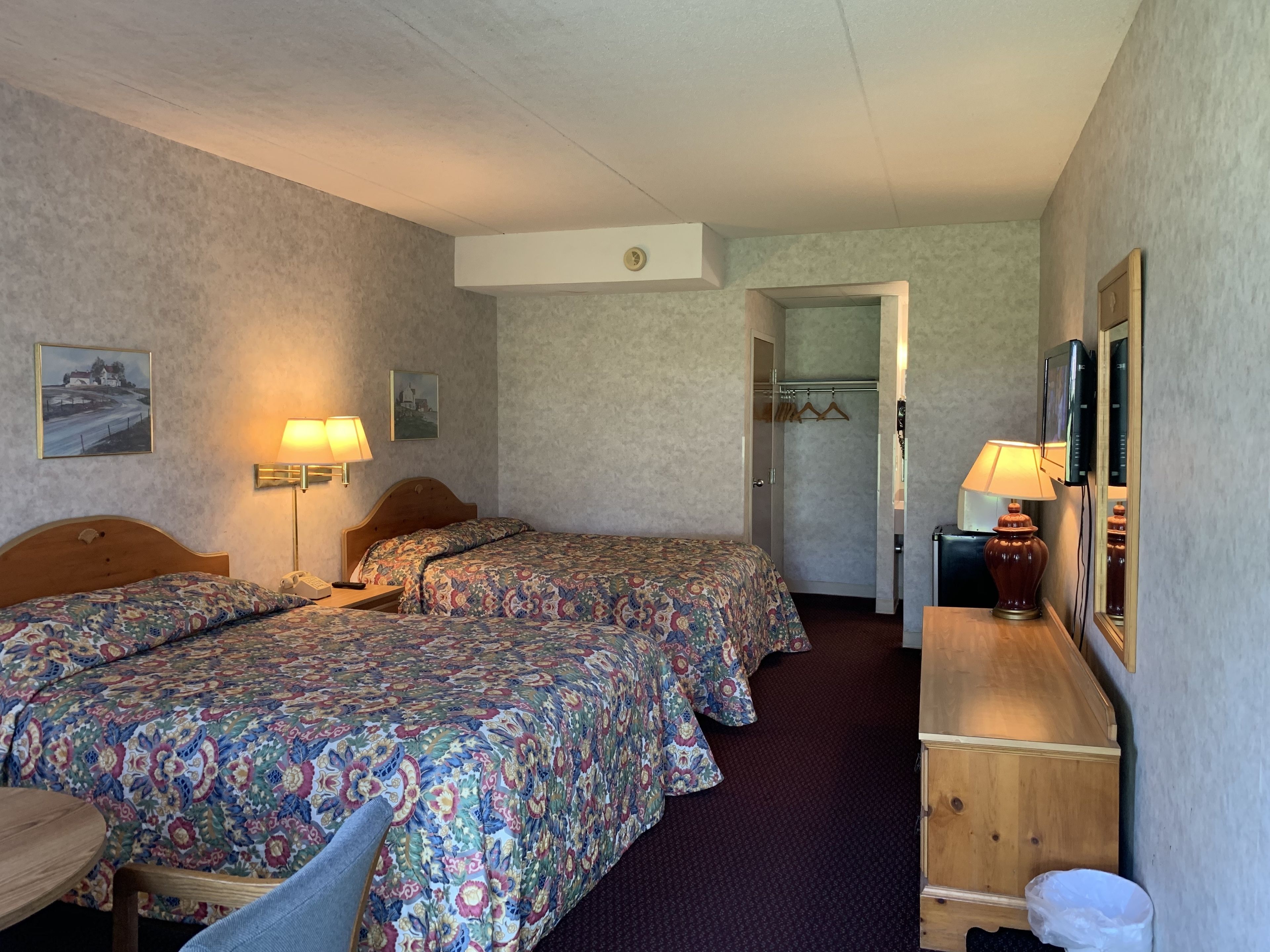 A hotel room with two beds, a wooden dresser, a mirror, and a television.