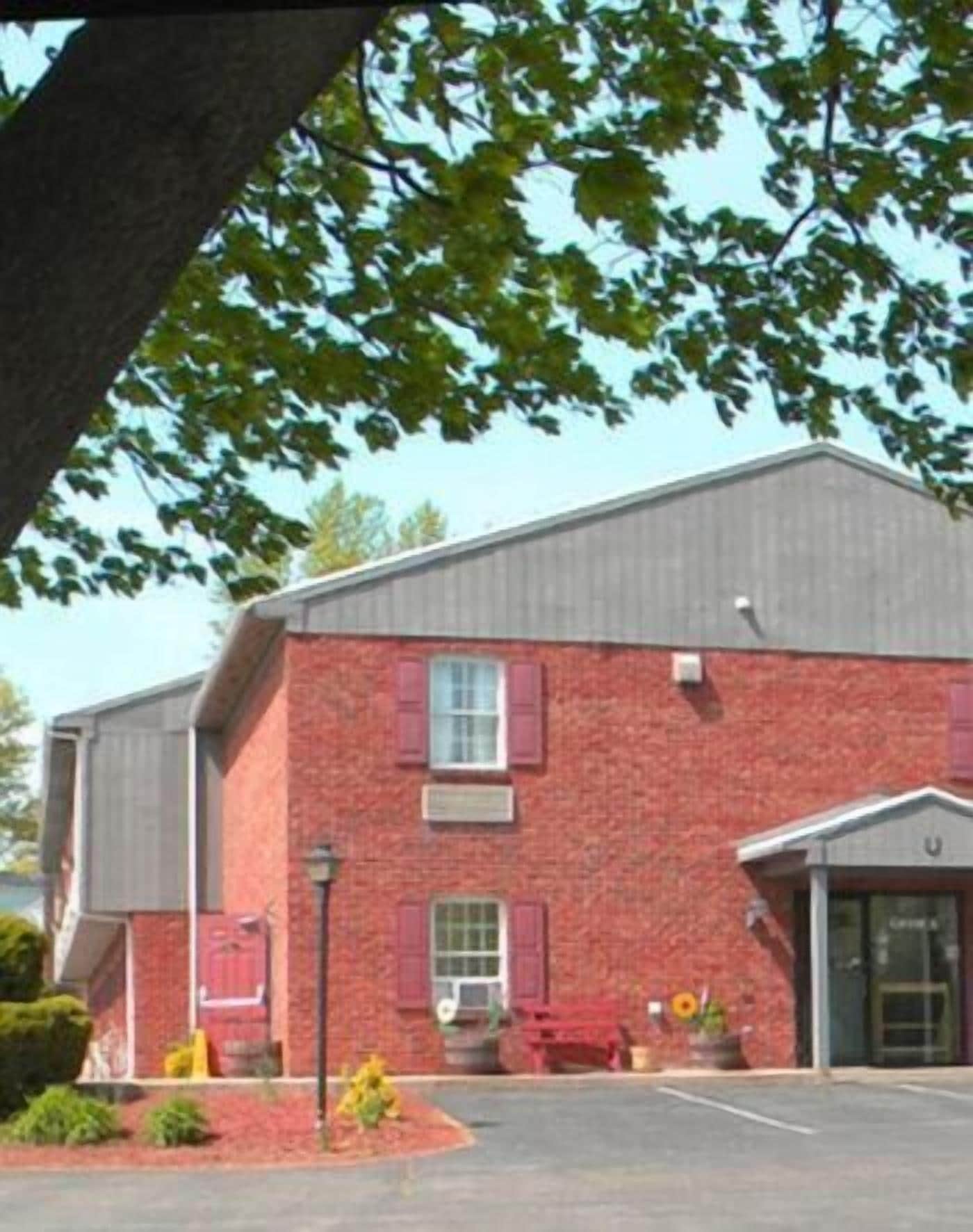 A red brick building with a flat roof, a central entrance with a door, and a small porch area with a bench.