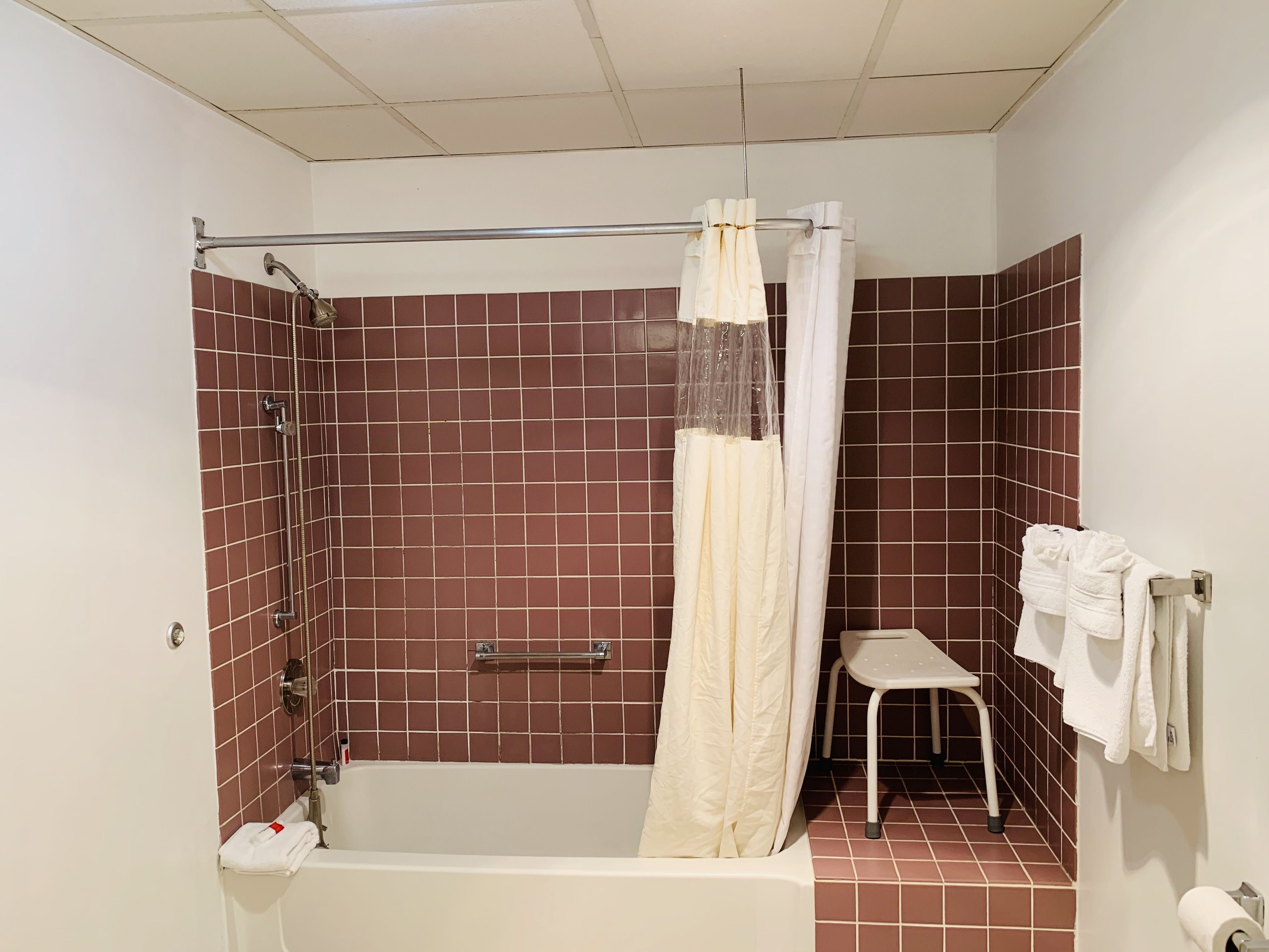 A bathroom with a bathtub, shower, and a small stool.